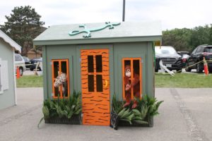 The second-place playhouse, a jungle green with orange accents, plastic ferns in the front and a lizard cut out of wood on the roof.
