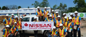 Nissan Canada Foundation members pose with a sign with their logo, wearing construction vests and hard hats with a pickup truck.