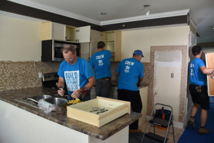 A crew of four is seen dismantling and removing a kitchen; also known as kitchen deconstruction