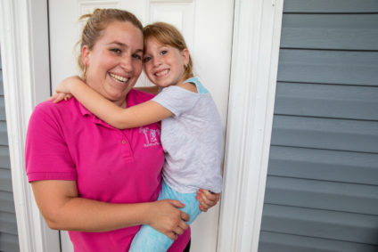 Smiling mother carrying and hugging her daughter at a Habitat for Humanity house