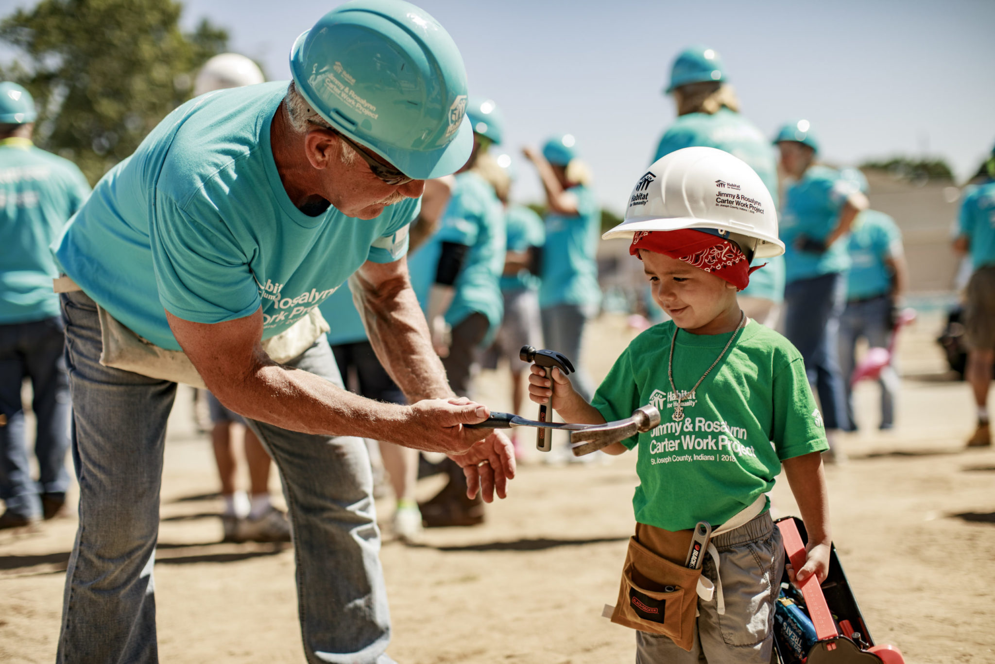 A gentleman exchanges hammers with a boy at a Habitat for Humanity home build
