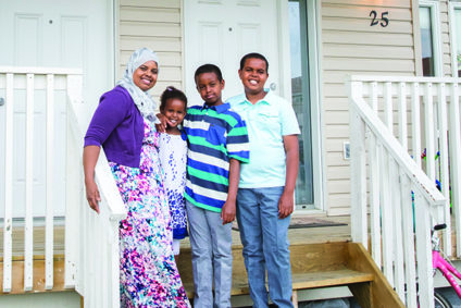 A Habitat for Humanity family of four are smiling in front of their home