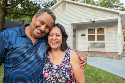 A man and woman in a warm embrace and smiling in front of their Habitat for Humanity home