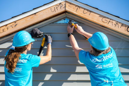 Two people finishing the house's wall siding by the gable at a Habitat for Humanity home