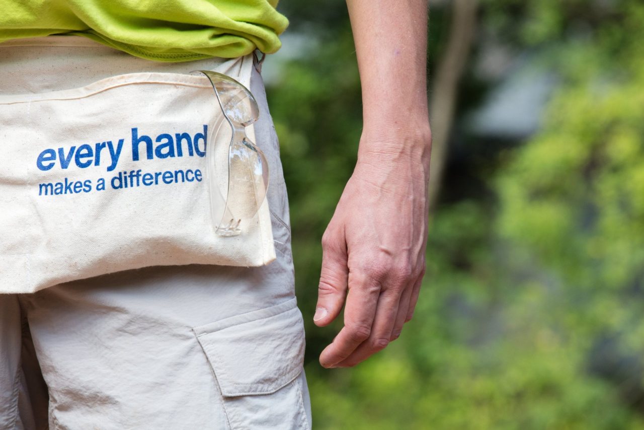 A person's arm and hand, with a sign on his fanny pack, "every hand makes a difference"